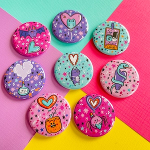May include: Eight colorful round pins with various designs. The pins feature a variety of themes, including hearts, animals, and whimsical characters. The pins are perfect for adding a touch of personality to bags, jackets, or other accessories.