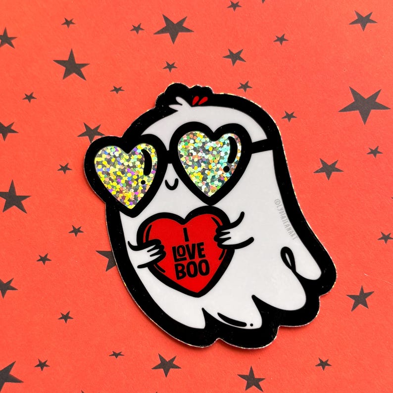 May include: A white ghost sticker with black outlines, wearing heart-shaped sunglasses with glittery lenses. The ghost holds a red heart with the words "I LOVE BOO" in white. The background is red with black stars.