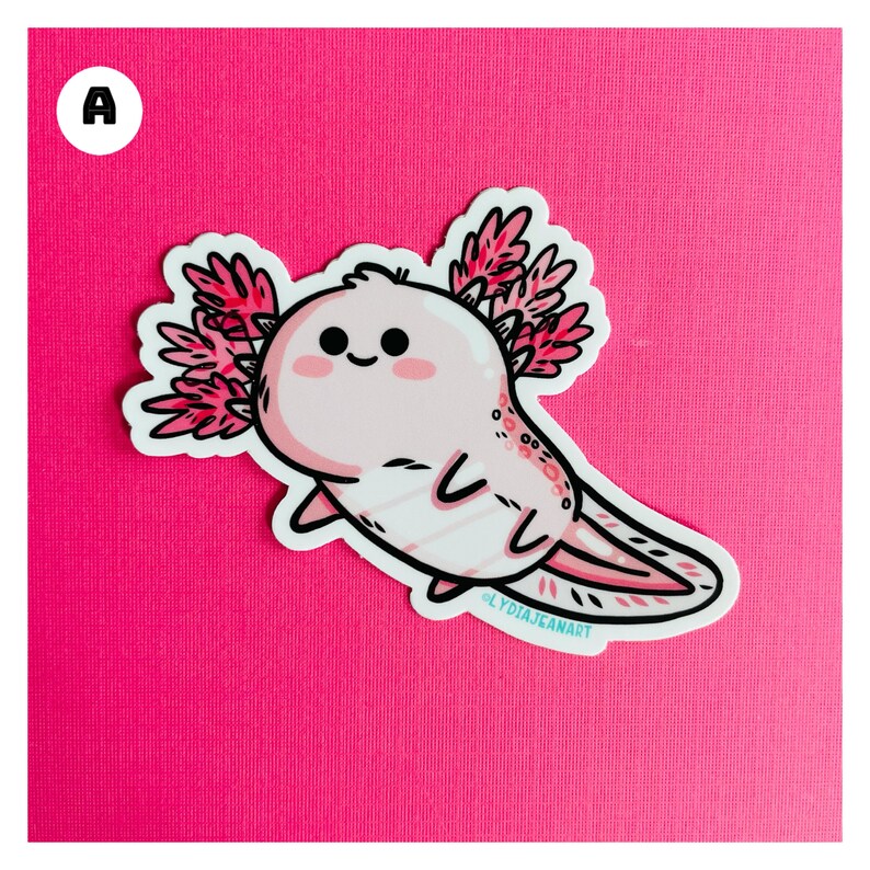 Puede incluir: Una pegatina rosa de ajolote con un contorno blanco y branquias rosas. El ajolote est&aacute; sonriendo con los ojos cerrados. La pegatina tiene el texto "@LYDIAJEANART" en la parte inferior.