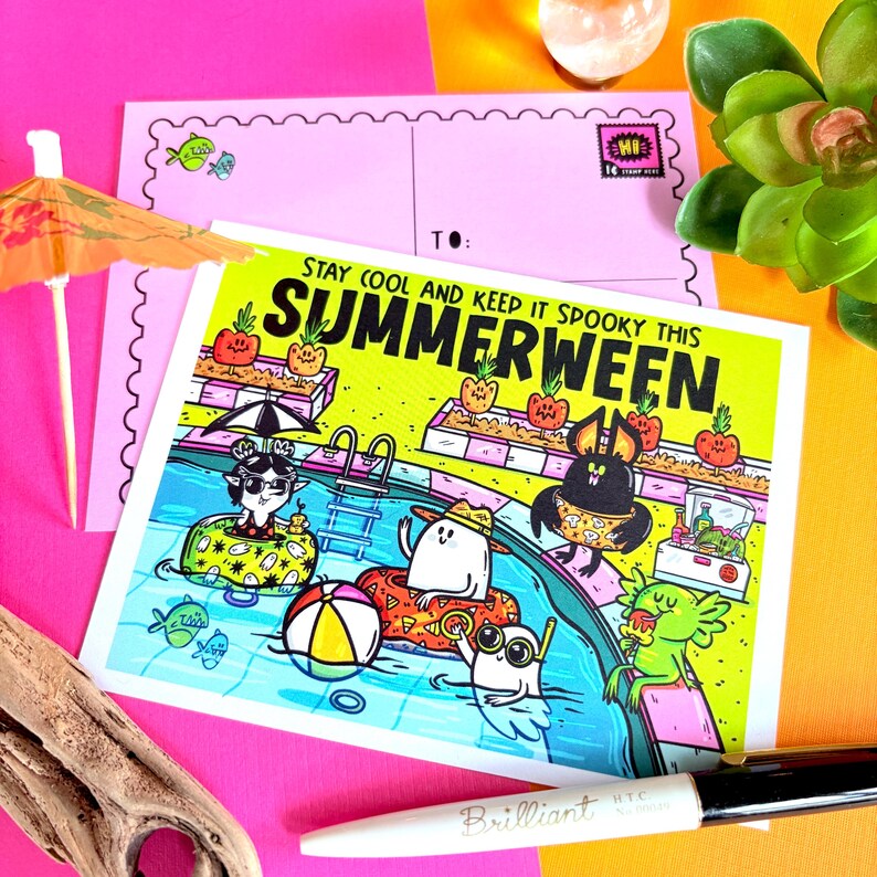 May include: A colorful postcard with the text "Stay Cool and Keep It Spooky This Summerween" featuring cartoon characters in a swimming pool. The postcard is on a pink background with a pen and a miniature umbrella.