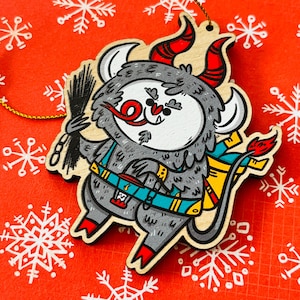 May include: A wooden Christmas ornament shaped like a gray monster with red horns, a red tongue, and a yellow and blue backpack. The monster is holding a black chimney brush.