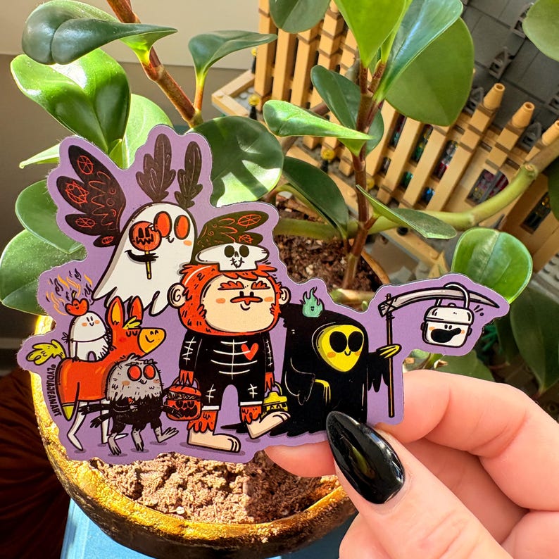 May include: A purple sticker featuring a group of cartoon Halloween characters. The characters include a ghost, a skeleton, a grim reaper, and other spooky creatures. The sticker is held in front of a plant.