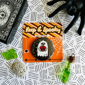 May include: A black and white button with a ghost holding a pumpkin. The button has a sparkly background and says "Keep it Spooky" on the packaging.