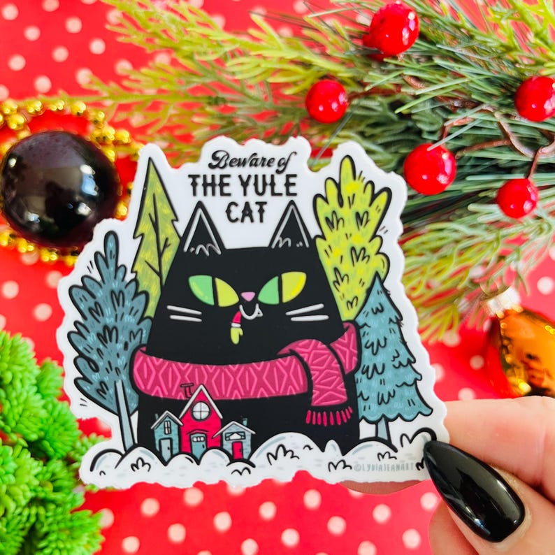 May include: A white sticker with a black cat wearing a pink scarf and the text "Beware of the Yule Cat" in a colorful font. The cat is surrounded by green and blue trees.