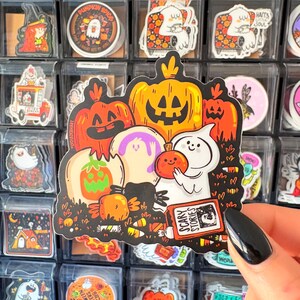 May include: A colorful Halloween sticker featuring pumpkins, ghosts, and candy corn. The sticker includes the text "SCARY STORIES" on a book. Other stickers with Halloween themes are visible in the background.