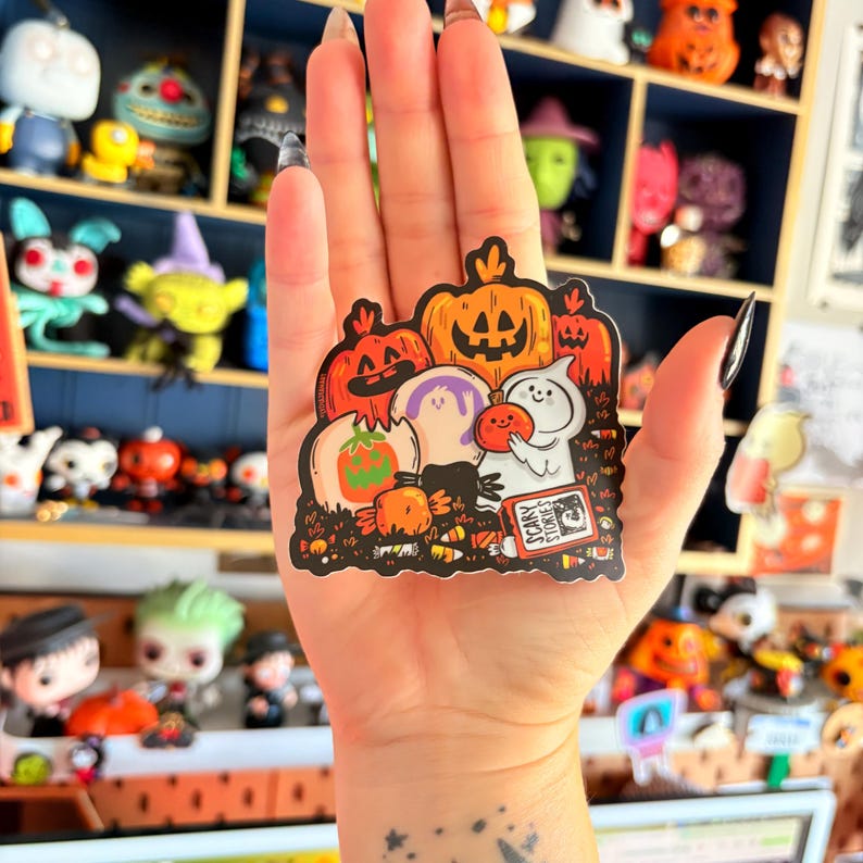 May include: A Halloween-themed sticker featuring pumpkins, ghosts, and the text "Scary Stories." The sticker has a black border and a variety of orange, white, and purple colors. The design includes a ghost holding a small pumpkin.