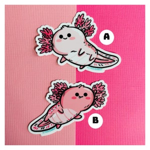 Puede incluir: Dos pegatinas de axolotl rosas con un contorno blanco y detalles rosas y blancos. Los axolotls sonr&iacute;en con la boca cerrada y tienen ojos peque&ntilde;os y negros. Las pegatinas est&aacute;n sobre un fondo rosa. Las pegatinas est&aacute;n etiquetadas con A y B.