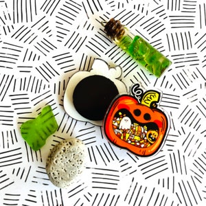 May include: A set of four Halloween-themed enamel pins. The pins feature a pumpkin with candy, a ghost, a black cat, and a witch's hat. The pins are all in a cartoon style and are perfect for adding a touch of Halloween fun to your clothing or bags.