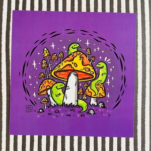 May include: A purple background with a cartoon illustration of a mushroom with a yellow top and a white stem. The mushroom is surrounded by smaller mushrooms and green creatures with long tails. The illustration is surrounded by a black circle with white stars.