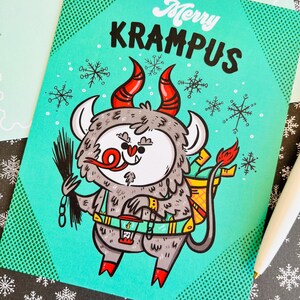 May include: A teal blue greeting card with a cartoon illustration of Krampus, a Christmas demon, with red horns, a chain, and a lantern. The card has a white polka dot pattern and the text "Merry Krampus".