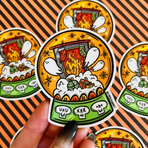 May include: A round, colorful sticker with a snow globe design. The snow globe contains a fireplace with stockings, a fire, and ghosts. The base of the snow globe is green and has the words "UUU" and "XXX" on it.