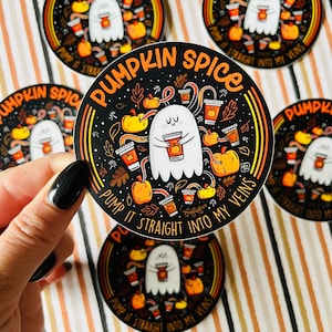 Puede incluir: Una pegatina redonda con fondo negro y un fantasma blanco sosteniendo una taza de café. La pegatina dice "Pumpkin Spice Pump It Straight Into My Veins" en una fuente amarilla y naranja.