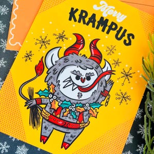 May include: A yellow Christmas card with a cartoon illustration of Krampus, a mythical creature with horns, a red ribbon, and a holly wreath. The card reads "Merry Krampus".