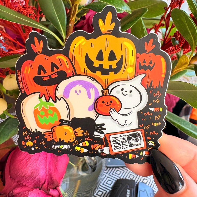 May include: A Halloween-themed sticker featuring cartoon pumpkins, ghosts, and candy corn. The sticker includes the text "Scary Stories" on a small book. The pumpkins are orange and yellow with carved faces.