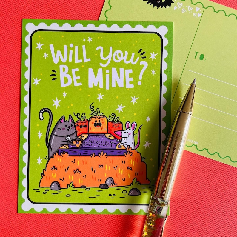 May include: A green postcard with the text "WILL YOU BE MINE?" and illustrations of a gray cat, pumpkins, and a white mouse. A gold pen and a blank postcard are also in the image. The postcard has a scalloped border and star accents.