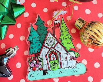 May include: A whimsical Christmas ornament featuring a cartoon house with a red roof, green door, and a chimney. The ornament has a ghost wearing a Santa hat and a black cat. The background is a red surface with white polka dots.