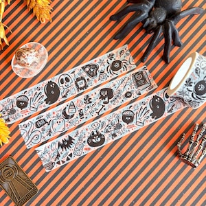 May include: Halloween-themed decorative washi tape with black and white illustrations of ghosts, spiders, and skulls. The tape features the text "Creep Real" and "Boo". The tape is on a striped orange and black background.