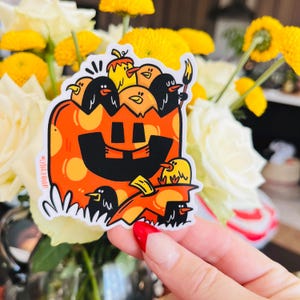 Puede incluir: Una pegatina con una calabaza de dibujos animados con una cara sonriente. La calabaza está llena de pequeños pájaros de dibujos animados, algunos de los cuales sostienen pinceles. La pegatina está sobre un fondo blanco.
