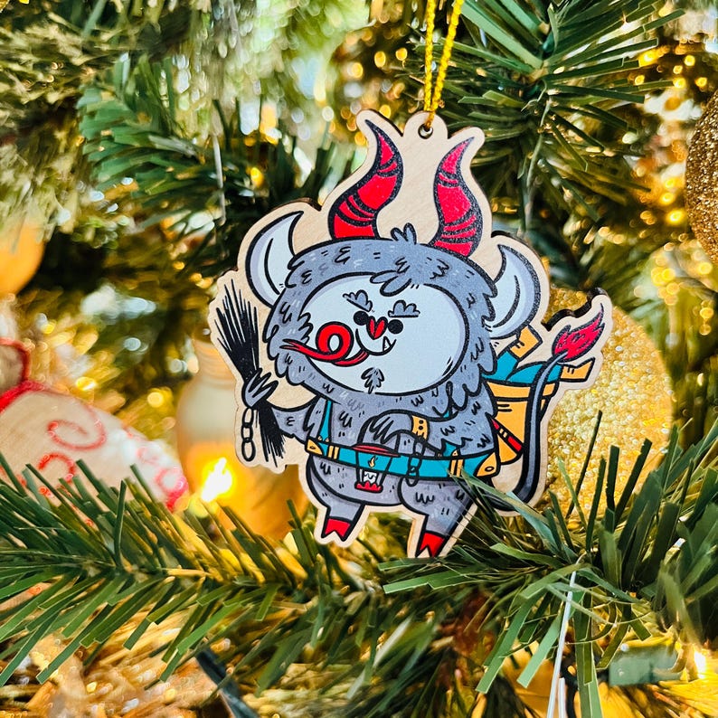 May include: A gray and red cartoon monster ornament with a red tongue sticking out, wearing a blue and yellow harness and carrying a broom. The ornament is hanging on a Christmas tree.
