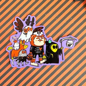 May include: A Halloween-themed sticker featuring a group of cartoon characters in costumes. The characters include a ghost, a skeleton, a grim reaper, and other creatures, all with a whimsical design. The sticker has a purple border and is set against an orange and black striped background.