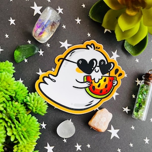 May include: A white ghost wearing sunglasses and eating a slice of watermelon. The ghost has a happy expression and is holding the watermelon with its hands. The background is a black and white pattern.