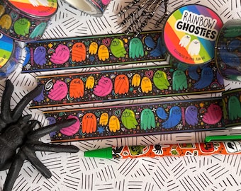 Puede incluir: Tres rollos de cinta washi Rainbow Ghosties con fantasmas de dibujos animados coloridos sobre un fondo negro, una mano de esqueleto plateada, una araña de plástico negra y un bolígrafo naranja con varios iconos e ilustraciones.