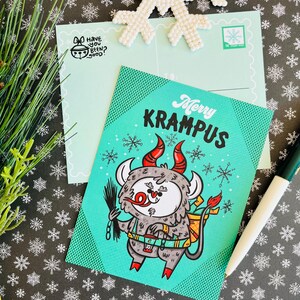 May include: A teal blue postcard with a cartoon illustration of Krampus, a Christmas demon, with red horns and a sack on his back. The text "Merry Krampus" is written in white letters on the postcard.