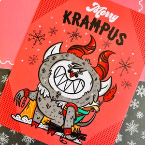 May include: A red greeting card with a white snowflake pattern. The card features a cartoon illustration of Krampus, a horned, furry creature with a mischievous grin. The text "Merry Krampus" is written in black lettering.