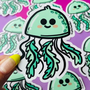 May include: A green and white cartoon jellyfish sticker with a smiling face and black eyes. The jellyfish has a round body and long, flowing tentacles.