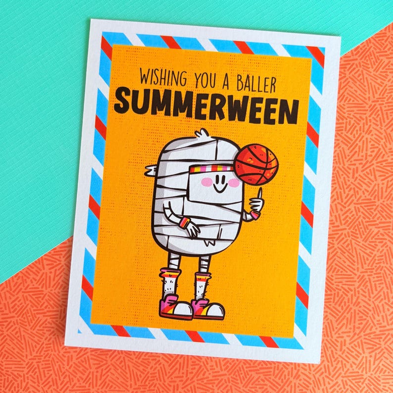 May include: Greeting card with a yellow background and a cartoon mummy holding a basketball. The card reads "Wishing you a baller Summerween" in black and white text. The card has a white border with blue and red stripes.