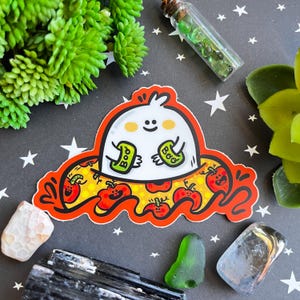 Op de afbeelding: Een witte geest met een vriendelijk gezicht houdt twee groene "Boo"-borden vast. De geest zit op een rood en oranje oppervlak met een pompoenpatroon.