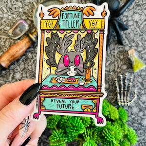Könnte beinhalten: Ein Aufkleber mit einem Cartoon-Glückstellerstand mit einem lila, mottenartigen Wesen im Inneren. Der Stand ist gelb und orange mit den Worten "Fortune Teller" auf der Vorderseite. Der Aufkleber sagt auch "Reveal Your Future".