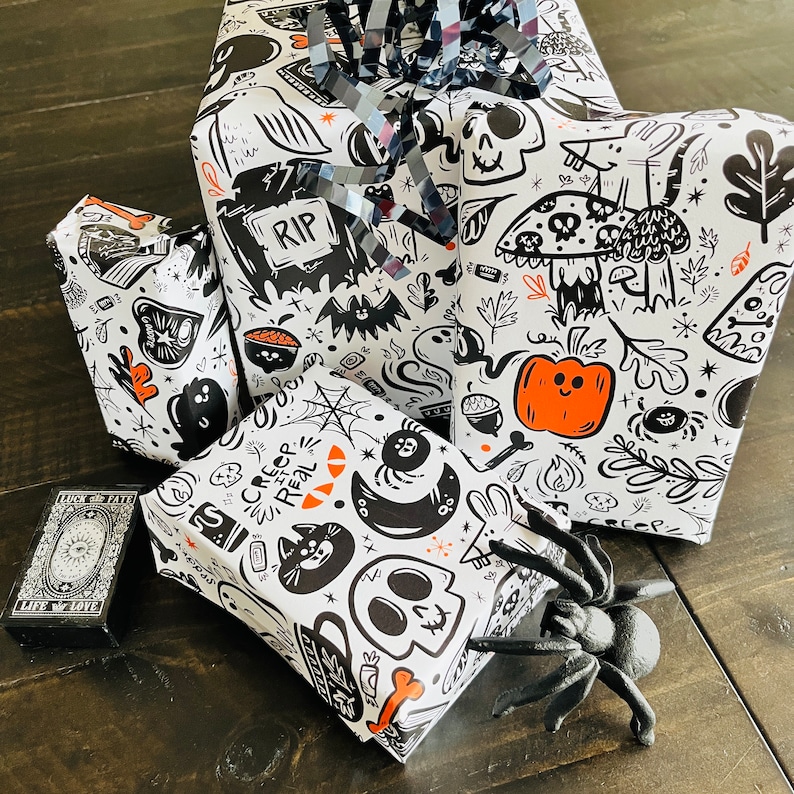 May include: Three black and white gift wrapping papers with spooky Halloween designs. One paper features a skull and crossbones, another has a ghost and bats, and the third has a spider and the words "Creep It Real".