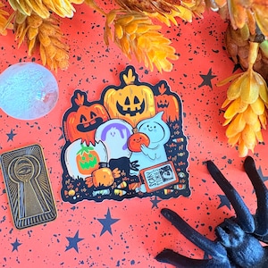 May include: A Halloween-themed sticker featuring cartoon pumpkins, ghosts, and candy. The sticker has the text "Scary Stories" on a small book. The background is orange with black stars and a black spider.