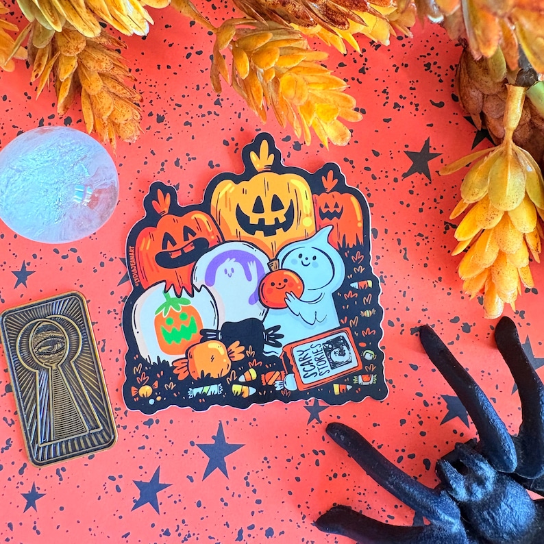May include: A Halloween-themed sticker featuring cartoon pumpkins, ghosts, and candy. The sticker has the text "Scary Stories" on a small book. The background is orange with black stars and a black spider.