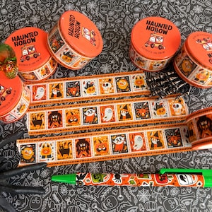 Puede incluir: Cuatro latas redondas de color naranja etiquetadas como Haunted Hollow y tres tiras de cinta decorativa washi con ilustraciones repetidas de personajes de Halloween, incluyendo fantasmas, calabazas y murci&eacute;lagos, junto a un bol&iacute;grafo estampado.