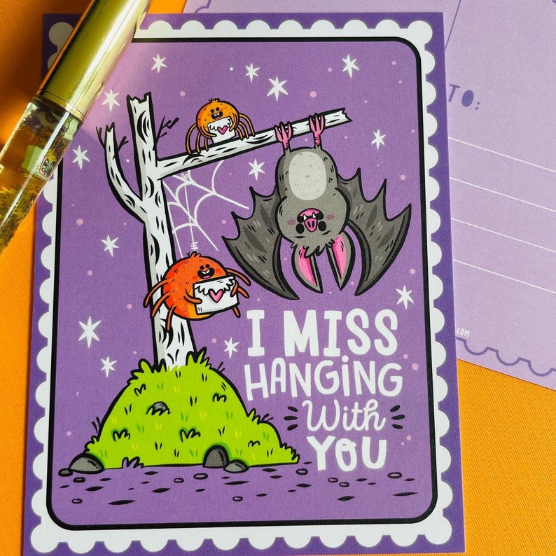 May include: A purple postcard with a cartoon bat hanging upside down and two spiders. The text "I MISS HANGING With YOU" is written in white. The postcard has a white scalloped border and is decorated with stars.