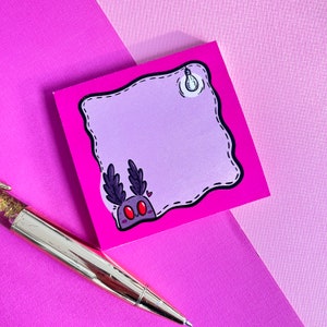 May include: A pink sticky note pad with a cartoon moth illustration. The moth has large red eyes and feathery antennae. The note pad has a light bulb illustration in the upper right corner and a decorative border.