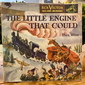 May include: Vintage RCA Victor record album cover for "The Little Engine That Could." The cover features a colorful illustration of a blue train, a giraffe, and other whimsical characters. The title and author's name are prominently displayed.