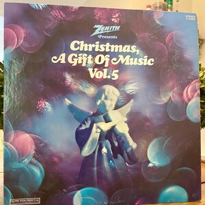 May include: A vintage vinyl record album cover with the text "Zenith Presents Christmas, A Gift Of Music Vol. 5." The cover features an illustration of an angel and a background of blue, pink, and white orbs.