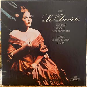 May include: A black vinyl record cover featuring a portrait of a person in a copper-colored off-the-shoulder gown. The text reads: VERDI La Traviata LORENGAR ARAGALL FISCHER-DIESKAU MAAZEL DEUTSCHE OPER BERLIN. The bottom right corner displays STEREO 60-5504 LONDON.