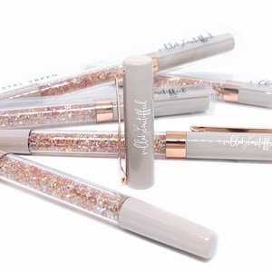 May include: A set of gray glitter pens with rose gold accents. The pens have the words "wildly beautiful" written on them.