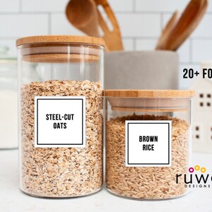 May include: Two glass jars with bamboo lids filled with steel-cut oats and brown rice. White labels with black text read "Steel-Cut Oats" and "Brown Rice".