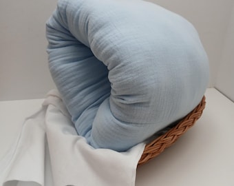 May include: A light blue, textured fabric blanket folded inside a woven wicker basket. A white cloth with a circular logo reading PURE COTTON STUDIO is draped over the edge of the basket, partially covering the light blue fabric.