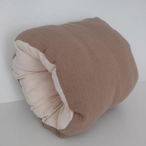 May include: A soft, rectangular cushion featuring a textured, taupe-coloured exterior fabric and a contrasting cream-coloured interior lining. The cushion is folded over itself, creating a rounded, tube-like shape that reveals both colour layers.
