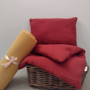 May include: A red and yellow set of bedding made of soft, textured fabric. The bedding is folded and placed in a wicker basket.