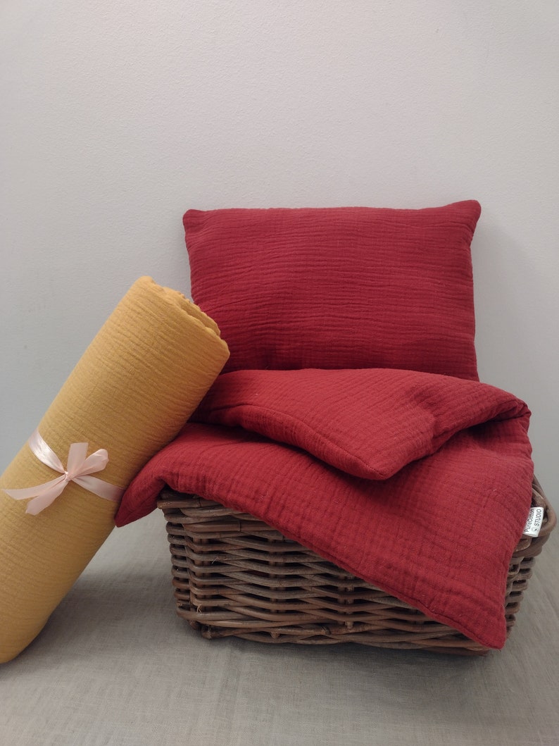May include: A red and yellow set of bedding made of soft, textured fabric. The bedding is folded and placed in a wicker basket.