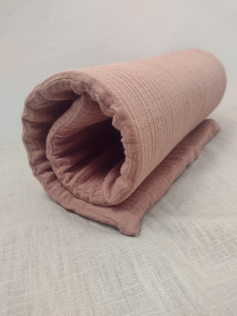 May include: A rolled up blush pink muslin swaddle blanket with a textured surface.