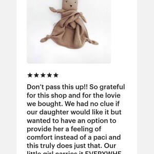 May include: A tan-colored bear-shaped security blanket made of soft, textured muslin fabric. The toy features a small bear head with embroidered eyes and nose, attached to a square piece of fabric with knotted corners for easy grasping.