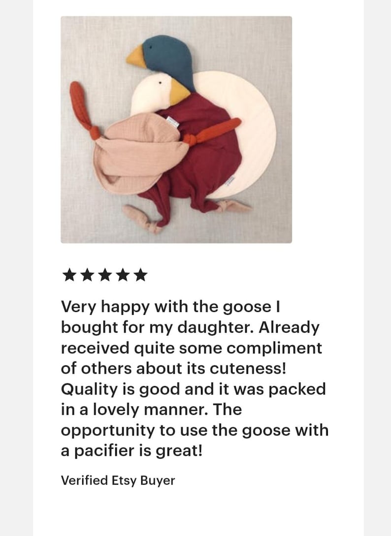 May include: A plush goose toy with a teal head, yellow beak, and burgundy body, paired with a smaller white goose. The toy includes a pacifier and is designed for babies and young children.